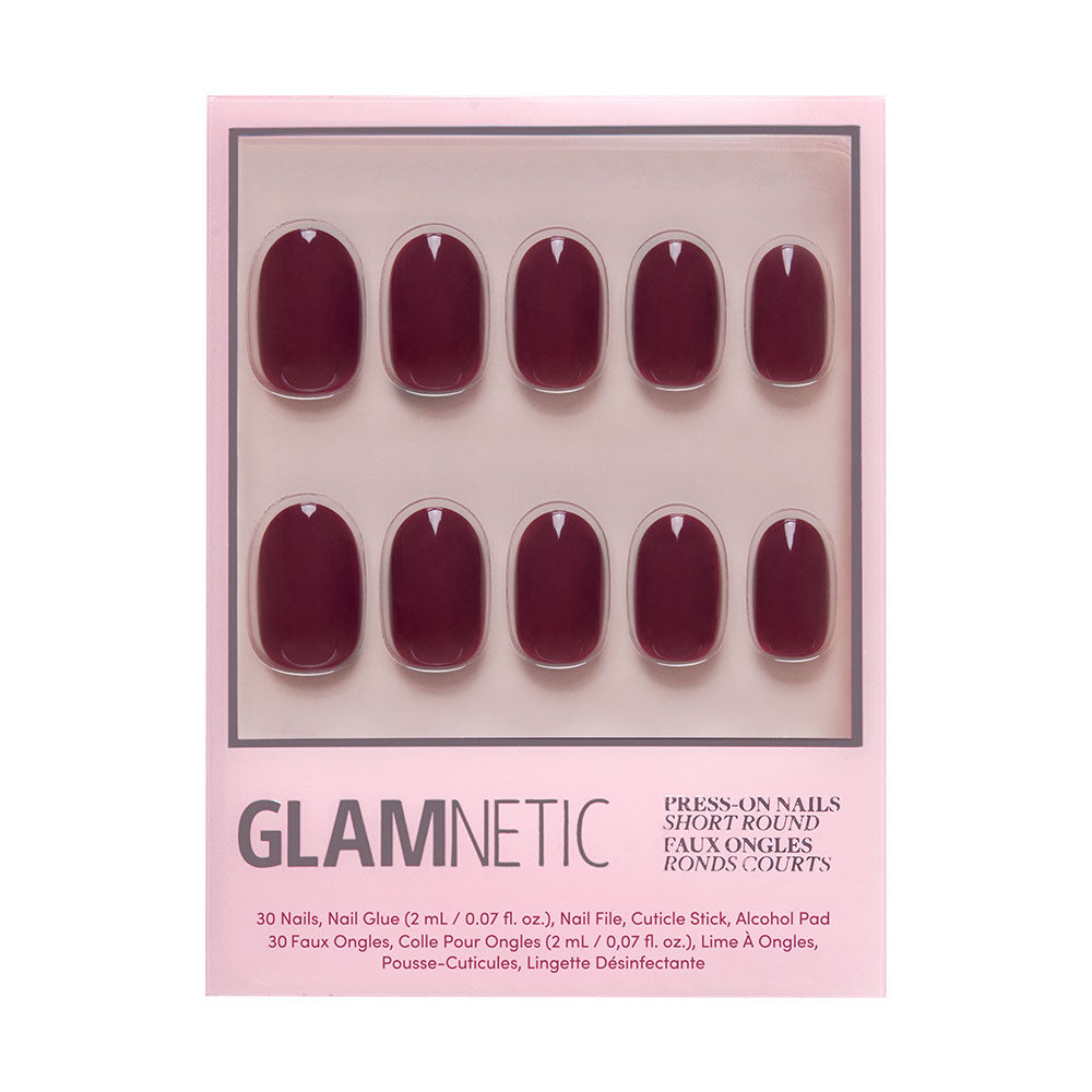 A set of 10 short, round, dark red Berry Maroon press-on nails by glamnetic displayed on pink packaging. The Fall Forest box includes nail glue, a cuticle stick, and an alcohol pad; product details are at the bottom.